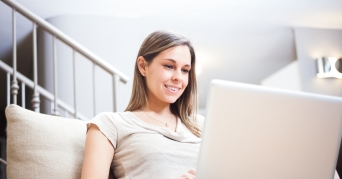 Frau schreibt auf Laptop auf Laptopkissen